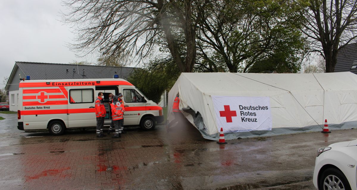 Ein Zelt und ein Wagen der Einsatzleitung des Deutschen Roten Kreuzes stehen auf einem verregneten Platz.