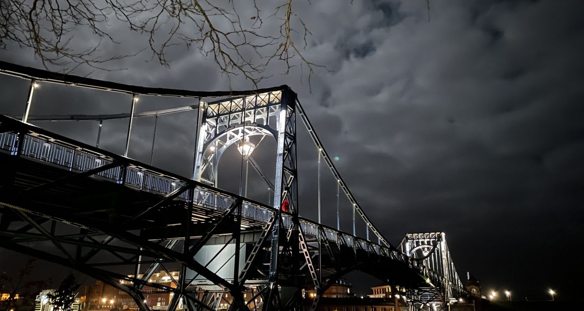 Das Foto zeigt die Kaiser-Wilhelm-Brücke vom Parkplatz vor dem Treppenaufgang aus. Es ist Nacht, bewölkt und der Mond scheint hell.