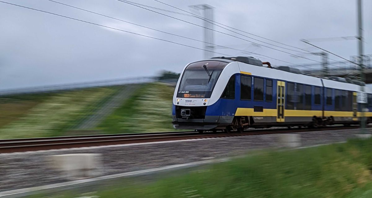 Ein Zug der NordWestBahn fährt mit hoher Geschwindigkeit durch Friesland.