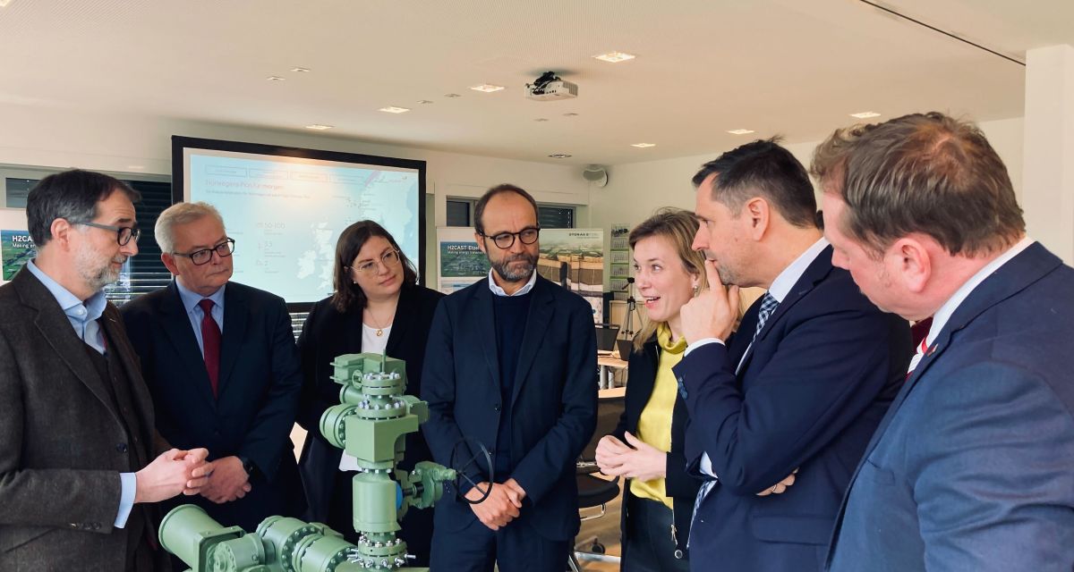 Zu sehen ist der norwegische Botschafter in Deutschland, Torgeir Larsen, bei einem Besuch in den Kavernenanlagen von Storag Etzel. Um ihn geringt stehen Vertreter*innen von Storag Etzel, der norwegischen Botschaft, Equinor, sowie Landes-, Bundes- und kommunaler Politik. Vor ihnen auf einem Tisch steht ein Modell von Rohrleitungen.