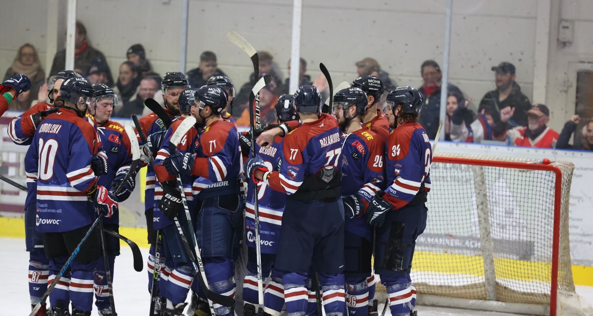 Eishockeyspieler des ECW Sande stehen vor einem Tor auf dem Eis.