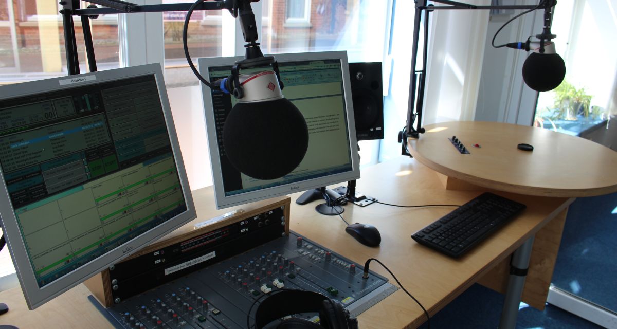 Das Radio Jade Studio in Jever mit zwei Computerbildschirmen, Mischpult, Kopfhörern und zwei Kugelmikrophonen an Galgen.