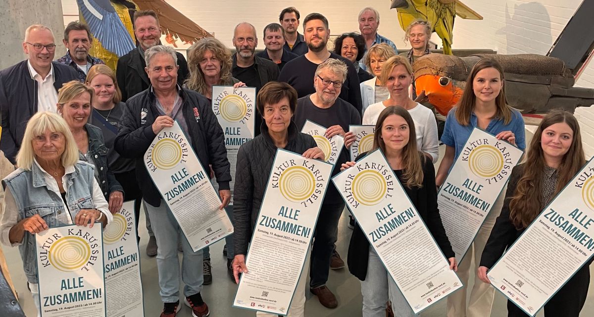 Akteur*innen des Kulturkarussells 2023 in Wilhelmshaven stehen mit Plakaten der Veranstaltung in der aktuellen Ausstellung der Wilhelmshavener Kunsthalle.