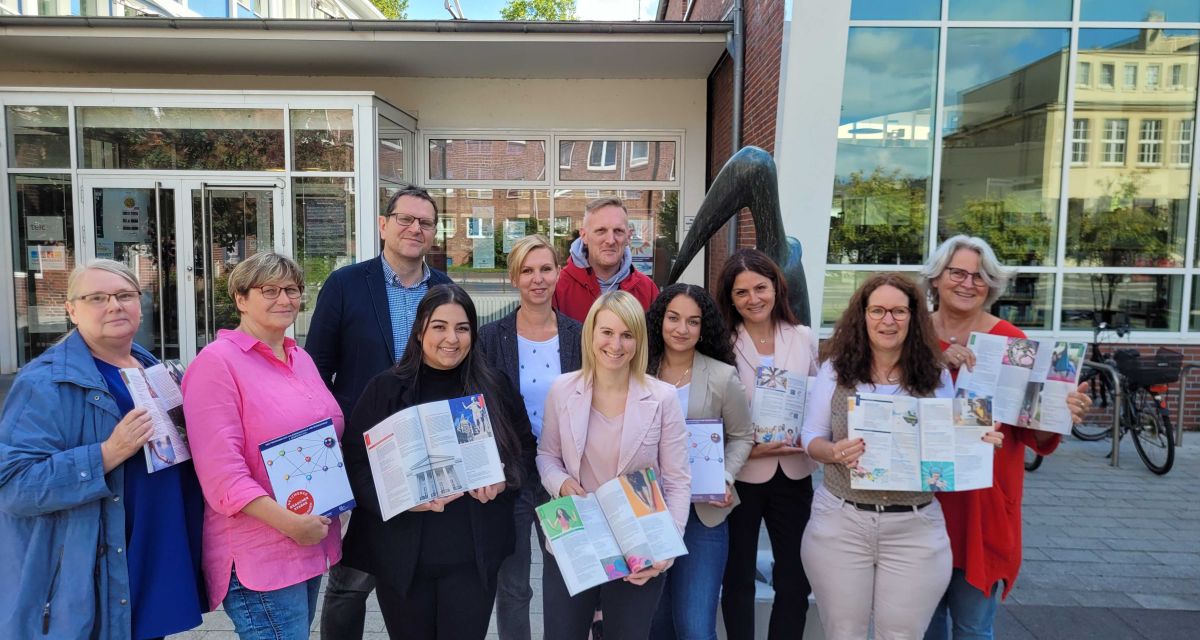 Vertreter*innen der Volkshochschule Wilhelmshaven präsentieren vor dem Eingang zur VHS und der Stadtbibliothek das neue Programm für 2023.