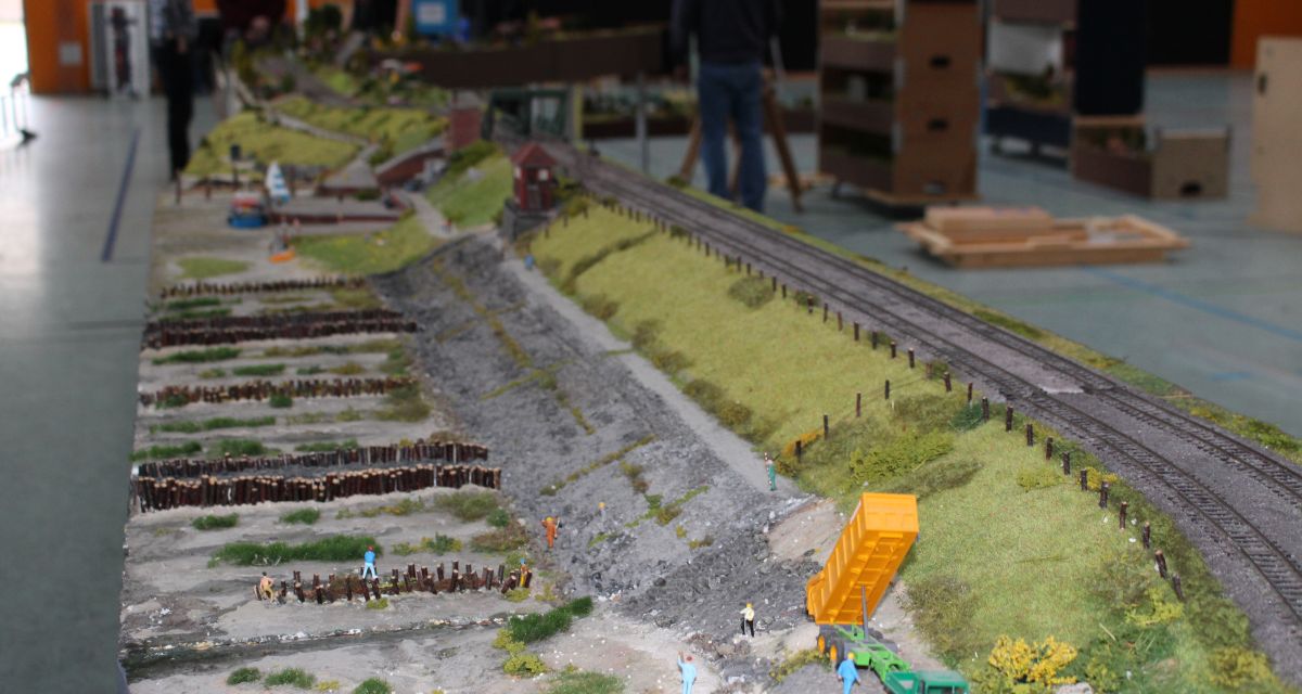 Die Eisenbahnfreunde Friesland e.V. veranstalten in der Sporthalle Heppens ihr 4. Internationales Friesentreffe der Modellbahner. Zu sehen sind Landschaften mit Modellbahnanlagen, im Hintergrund Vereinsmitglieder beim Aufbau.