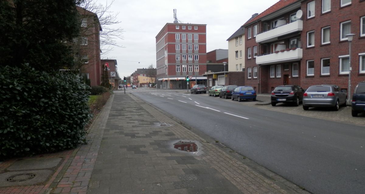 Gezeigt wird eine Straße mit Wohnhäusern und parkenden Autos