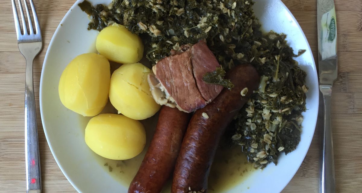 Ein Teller mit klassischem Grünkohlessen mit Pinkel, Kartoffeln und Grünkohl