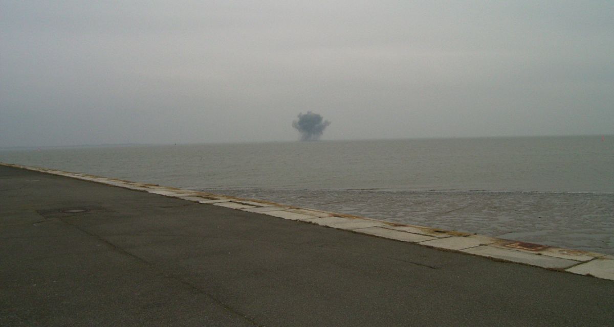 Zu sehen ist das Meer, in weiter Ferne sind die Spuren einer Sprengung erkennbar. 