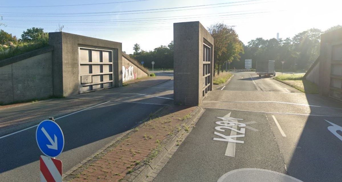 Zu sehen ist das Deichtor an der Flutstraße im Wilhelmshavener Stadtnorden. Das Tor ist geöffnet, im Hintergrund ist ein Lkw, im Vordergrund eine Verkehrsinsel zu sehen. Über das Tor spannt sich eine Hochspannungsleitung.