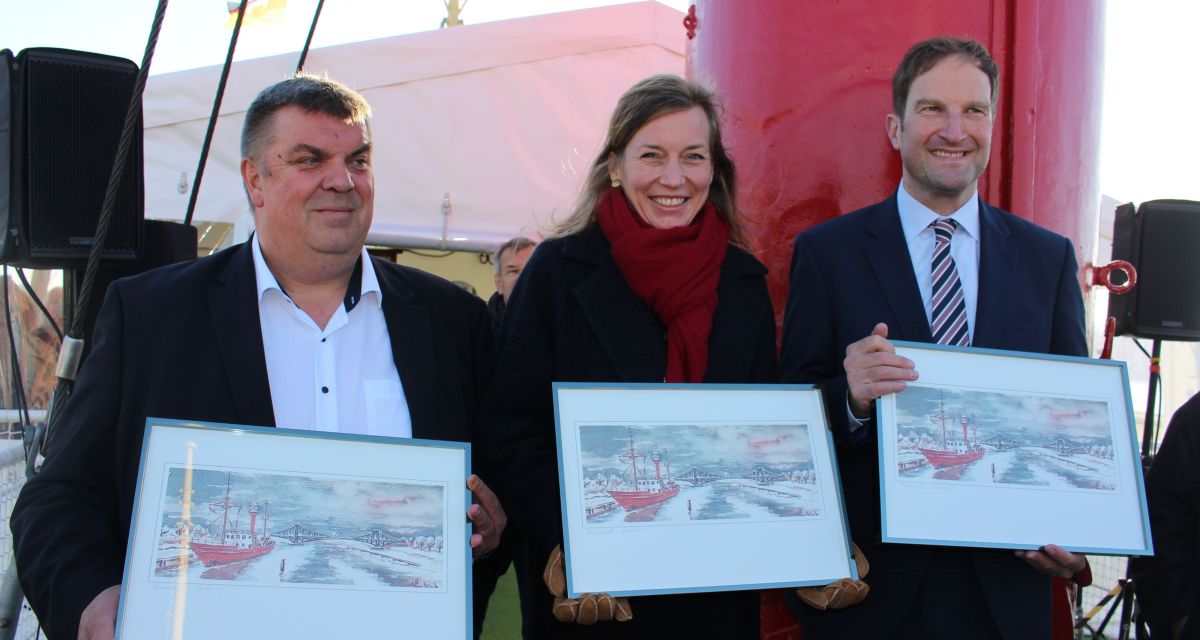 Zu sehen sind Bürgermeister Carsten Feist, Staatssekretärin Siemtje Möller und Stadtbaurat Nikša Marušić. Alle drei halten gerahmte Bilder in den Händen, auf denen das Feuerschiff Norderney zu sehen ist.
