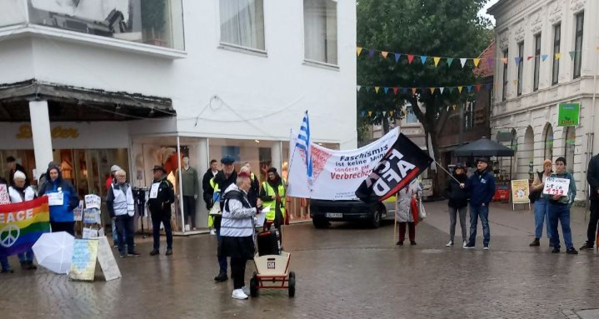 Teilnehmende der Mahnwache gegen rechts stehen im Halbkreis gegenüber einem Infostand der AfD. Oma gegen rechts, Erika, hält eine Ansprache.
