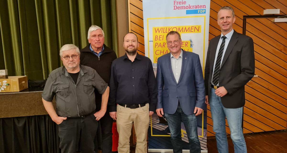Die FDP-Kreisverbände aus Friesland, Wilhelmshaven und Wittmund haben ihren Kandidaten für die Bundestagswahl 2024 gewählt. Robert Wegener aus Wilhelmshaven ist gemeinsam mit Wolfgang Sievers (Wittmund), Dr. Michael von Teichman (Wilhelmshaven), Hayo Sieckmann und Hendrik Theemann (beide Friesland) im Bürgerhaus Schortens zu sehen. Im Hintergrund steht ein Aufsteller der Partei, außerdem zu erkennen ist die Bühne des Bürgerhauses mit grünem Vorhang.