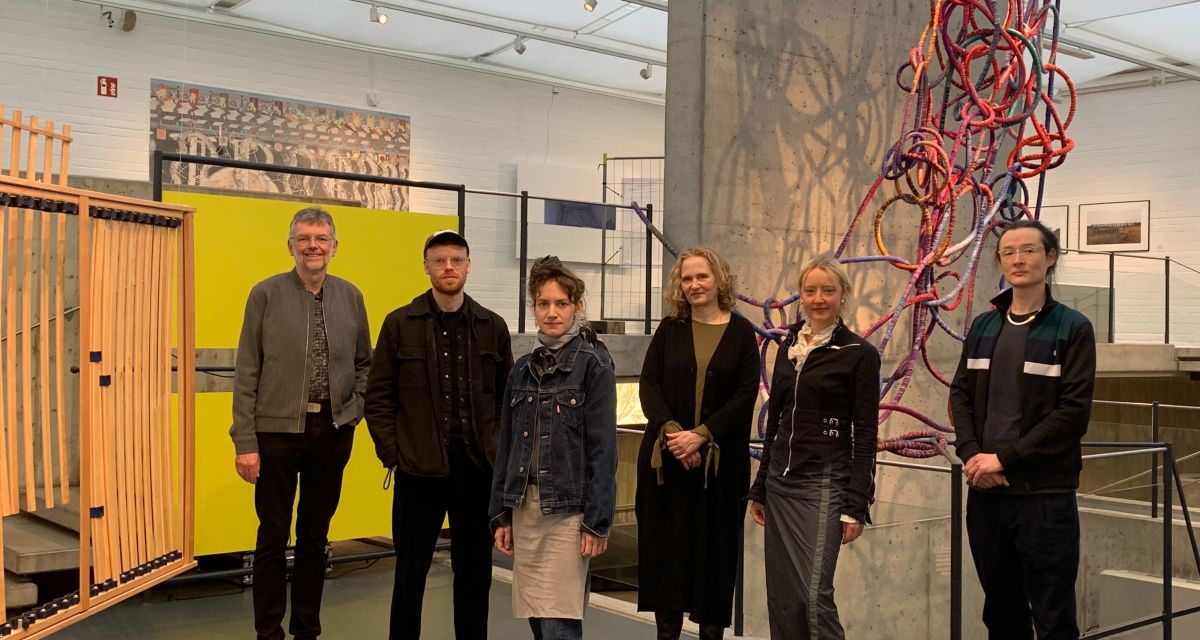 Auf dem Foto sind die Organisator*innen des Preises Nordwestkunst 2025 und einige der ausstellenden Künstler*innen zu sehen. Von links: Christoph Goritz (Verein der Kunstfreunde für Wilhelmshaven e.V.), Jakob Spengemann und Tina Henkel (beide ausstellende Künstler*innen), Petra Stegmann (Leiterin der Kunsthalle), Léonie von Saldern und Daniel Kuge (beide ausstellende Künstler*innen). Im Hintergrund sind einige der ausgestellten Werke in der Kunsthalle Wilhelmshaven zu sehen. 