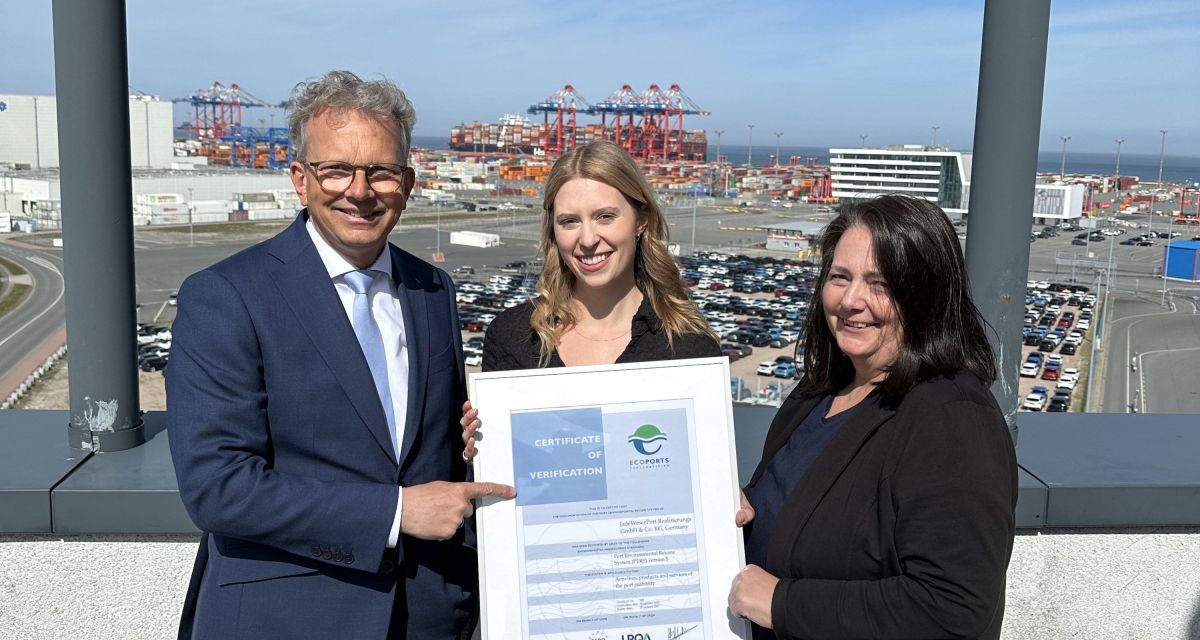 Die JadeWeserPort-Realisierungs GmbH & Co KG (JWPR) erhält die PERS-Umweltmanagement-Zertifizierung. Auf dem Foto mit dem Wilhelmshavener Tiefwasserhafen im Hintergrund sind zu sehen: Holger Banik, Geschäftsführer JWPR und NPorts, Denise Schablitzki, Strategische Unternehmensentwicklung NPorts und Silke Lüders, Umweltkoordinatorin JWPR. Sie halten gemeinsam die Zertifizierungsurkunde in Händen.