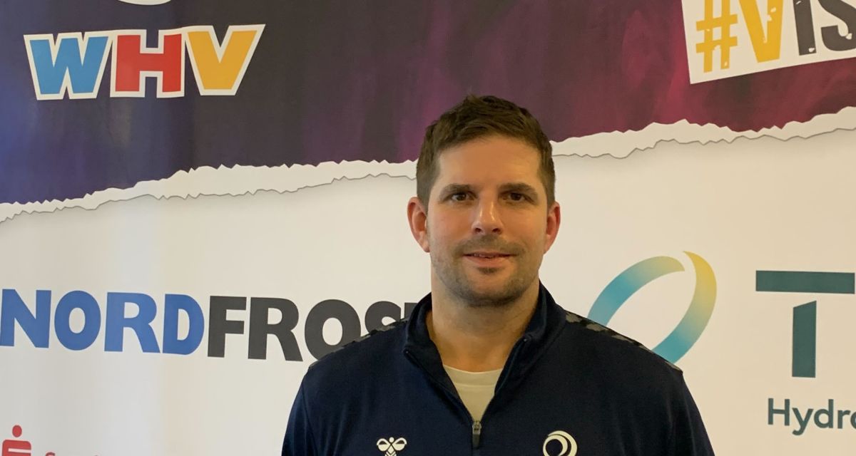 Der Trainer des Wilhelmshavener Handballvereins (WHV), Christian Köhrmann, steht vor einem Austeller mit den Logos der Sponsoren des WHV.