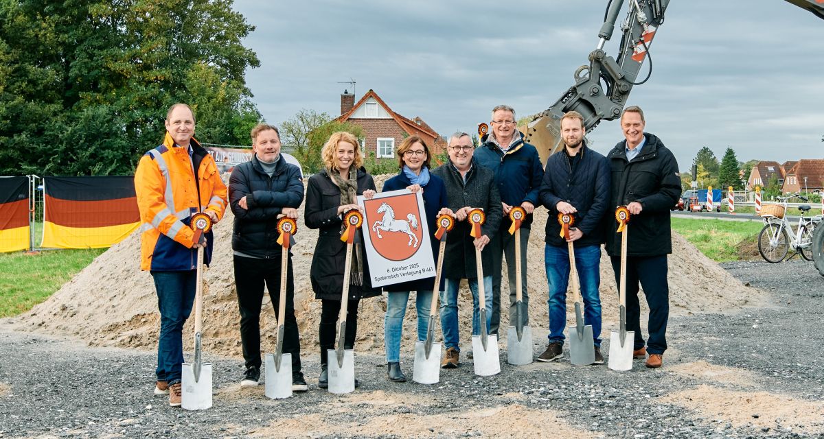 Der symbolische Spatenstich zur Verlegung der Bundesstraße B461 in Carolinensiel. Zu sehen sind unter anderem Wittmunds Landrat Holger Heymann, der Bürgermeister der Stadt Wittmund Rolf Claußen und die CDU-Landtagsabgeordnete Katharina Jensen. Die abgebildeten Personen halten Spaten mit schwarz-rot-goldenen Kokarden und dem Sachsenross. Im Hintergrund sind ein Sandhaufen und die Schaufel eines Baggers zu erkennen, an Bauzäunen ist die Flagge der Bundesrepublik angebracht. Zwei der Personen halten außerdem ein Schild mit dem niedersächsischen Landeswappen und der Aufschrift