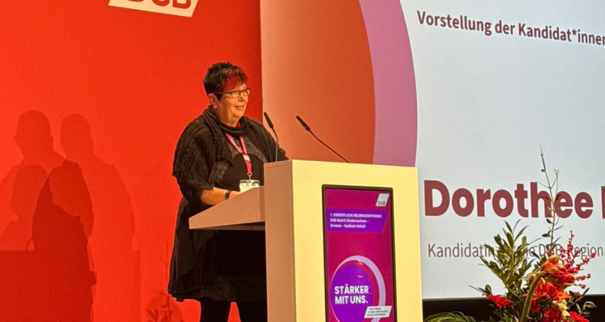 Dorothee Koch stellt sich auf der 7. Bezirkskonferenz des DGB Niedersachsen-Bremen-Sachsen-Anhalt zur Wahl als Geschäftsführerin der neu geschaffenen DGB-Region Weser-Ems. Sie wurde mit 96,3 Prozent der Stimmen gewählt. Koch mit kurzen roten Haaren und dunkler Kleidung steht an einem Rednerpult auf einer Bühne. Im Hintergrund ist das Logo des Deutschen Gewerkschaftsbundes zu sehen, auf dem Rednerpult ist ein violetter Kreis mit der Aufschrift