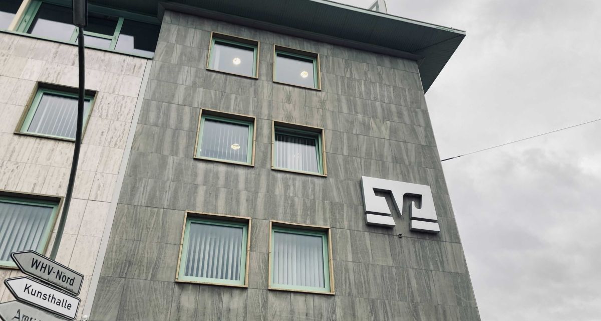 Zu sehen ist das Logo der Volksbanken und Raiffeisenbanken an der Hauptgeschäftsstelle der Volksbank Wilhelmshaven eG an der Ecke Peterstraße/Virchowstraße in Wilhelmshaven. Im linken unteren Bildrand zeigen Hinweisschilder in Richtung 