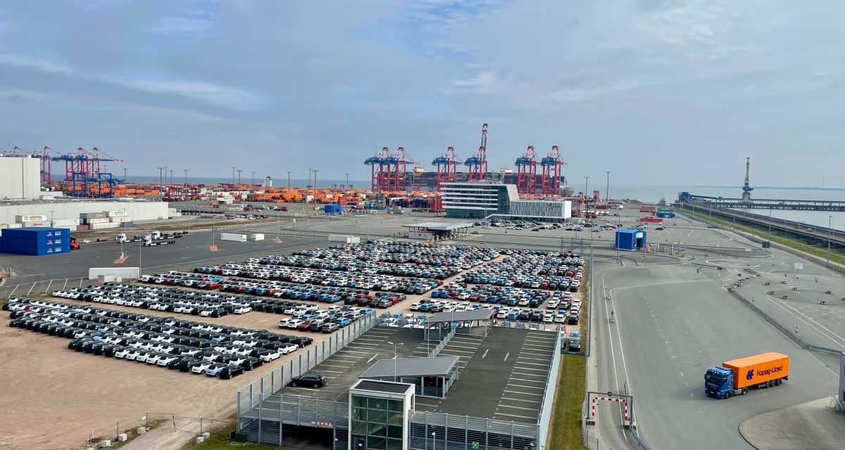 Zu sehen ist ein Hafengelände mit Autuumschlagsplätzen und Containerbrücken aus erhöhter Perspektive