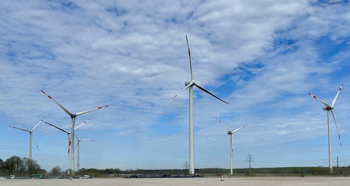 Zu sehen sind Windräder vor einer sandigen Fläche.