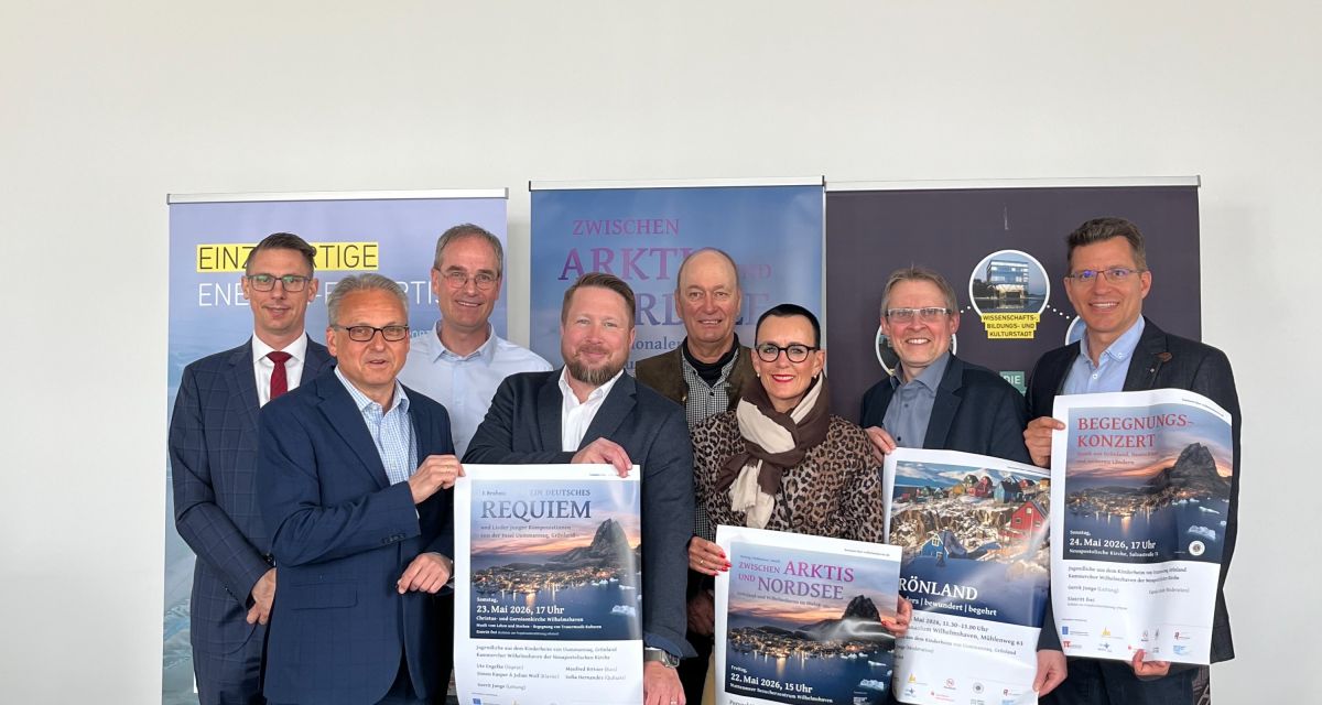 Zu sehen sind die Organisator*innen und Unterstützer*innen des Internationalen Kulturaustausches mit Grönland und Wilhelmshaven beim Vorabtermin im Wilhelmshavener Ratrium. Sie halten die Plakate zu den 4 Veranstaltungen des Austausches am Pfingstwochenende 2026 hoch. 