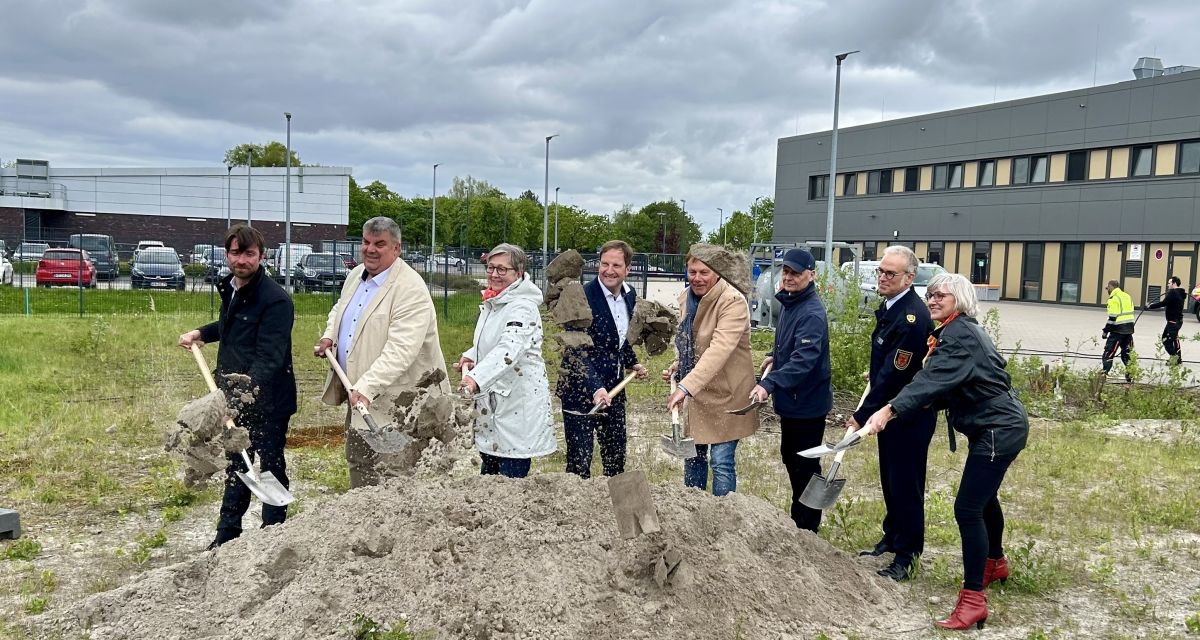 Zusehen sind vor einem Haufen Sand mit Spaten gerüstet verschieden Funktionsträger.