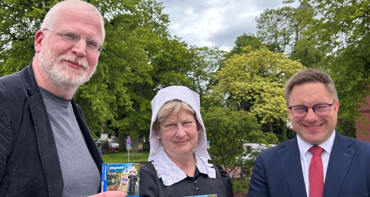 Die Playmobil-Figur von Maria von Jever wird vorgestellt. Mit dem verpackten Spielzeug in der Hand sind zu sehen (von links): Dr. Matthias Bollmeyer (Ratsmitglied und Initiator), Elisabeth Wilken als Fräulein Maria und Bürgermeister Jan Edo Albers.