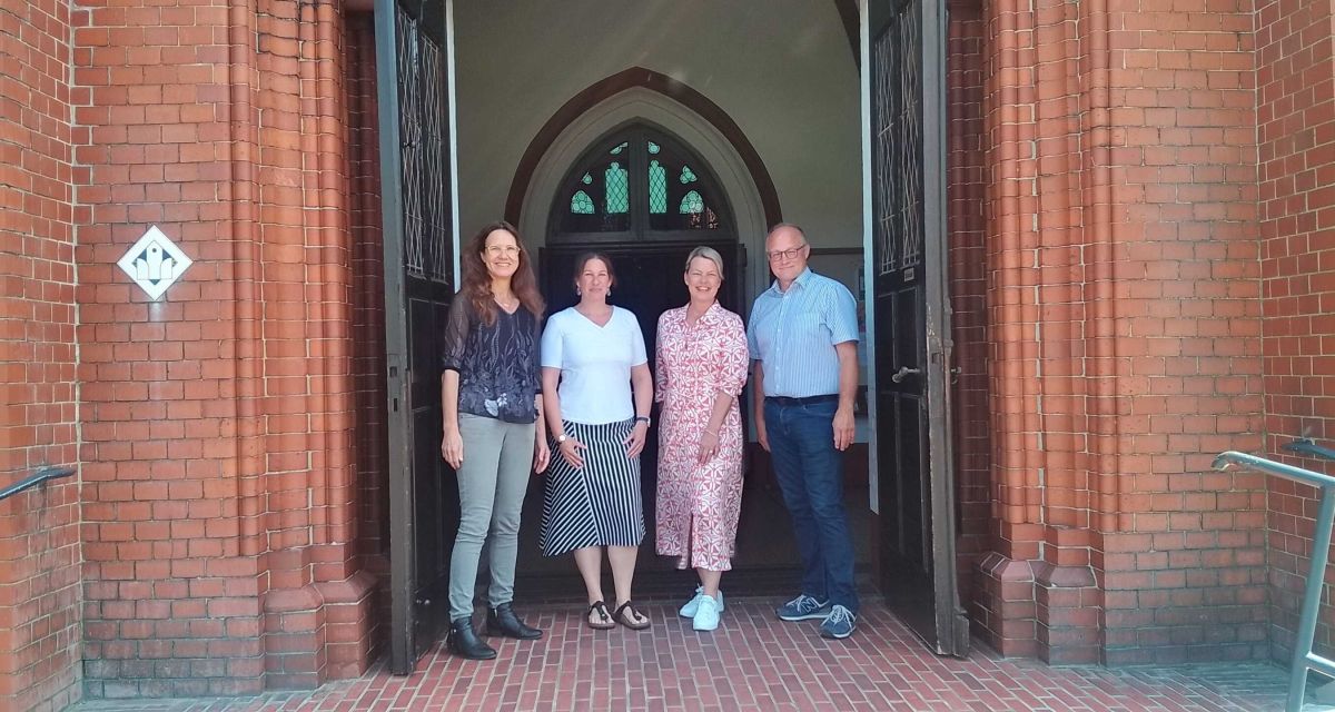 Im Portal der Banter Kirche in Wilhelmshaven stehen (von links) Pastorin Anke Stalling, Freia Bergenthum (Leiterin Kita Bant I), Katrin Draschar (Leiterin Kita Bant II) und Hendrik Rösing (Leiter des Kitaverbundes Wachsen & Werden)