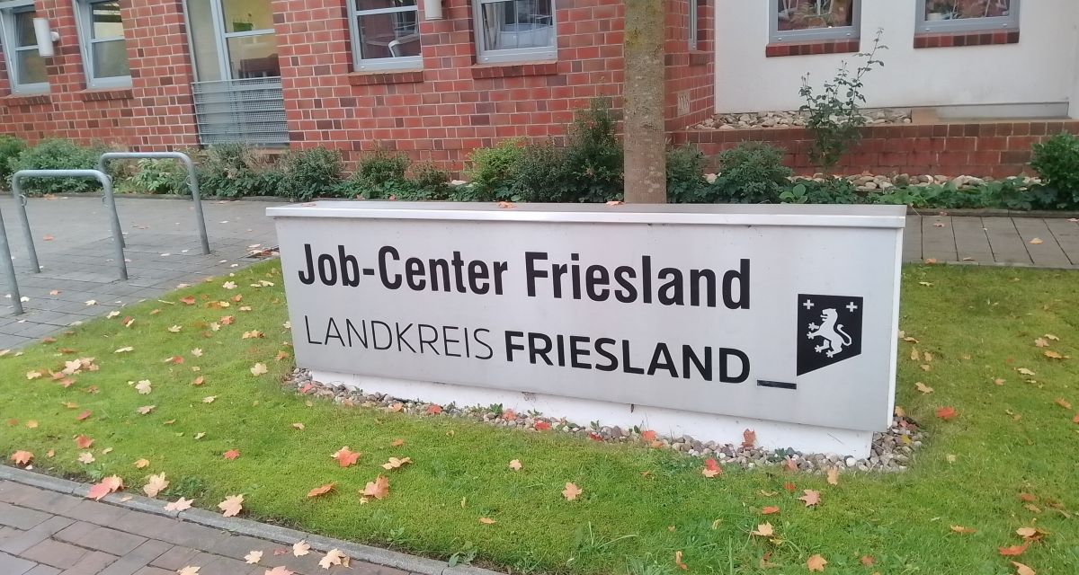 Zu sehen ist das Hinweisschild des Jobcenters in Jever. Auf der grauen Metalstele steht