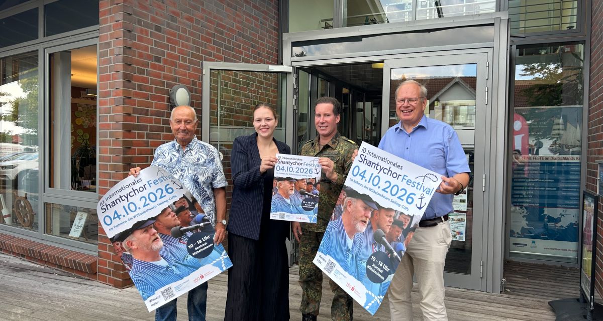 Helmut Möhle, Virginia Berg, Sebastian Uhle und Frank Moritz stehen vor dem Gebäude der Wilhelmshaven Touristik und Freizeit und halten Plakate zum 10. Internationalen Shantychor-Festival hoch.