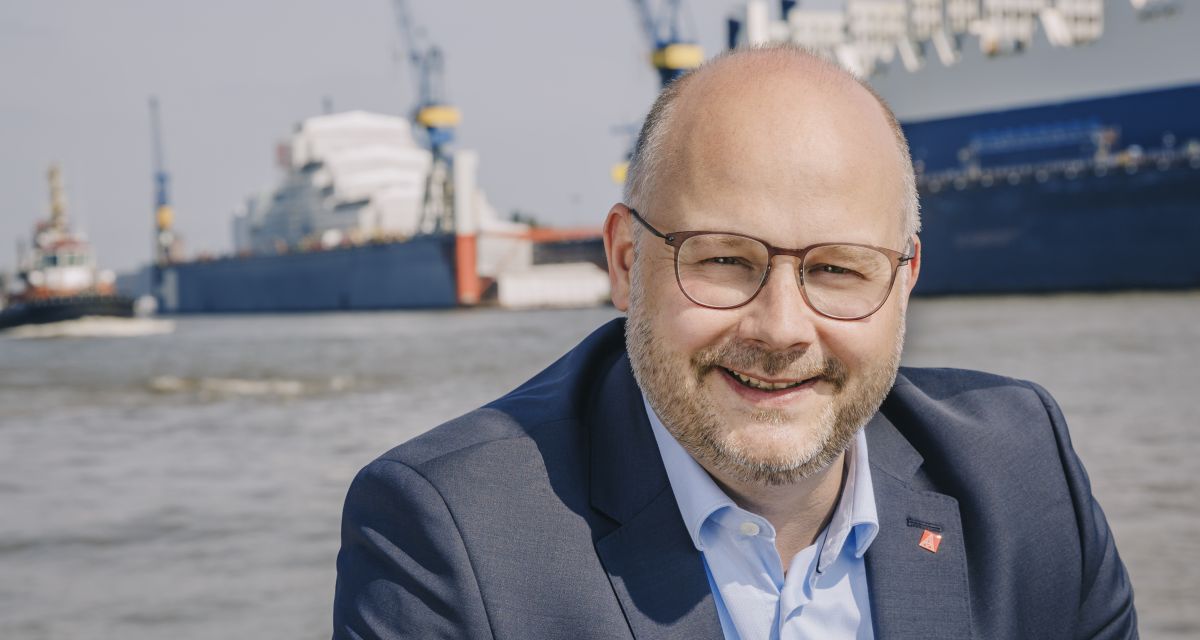 Der Bezirksleiter der IG Metall Küste Daniel Friedrich vor einer Hafenkulisse.