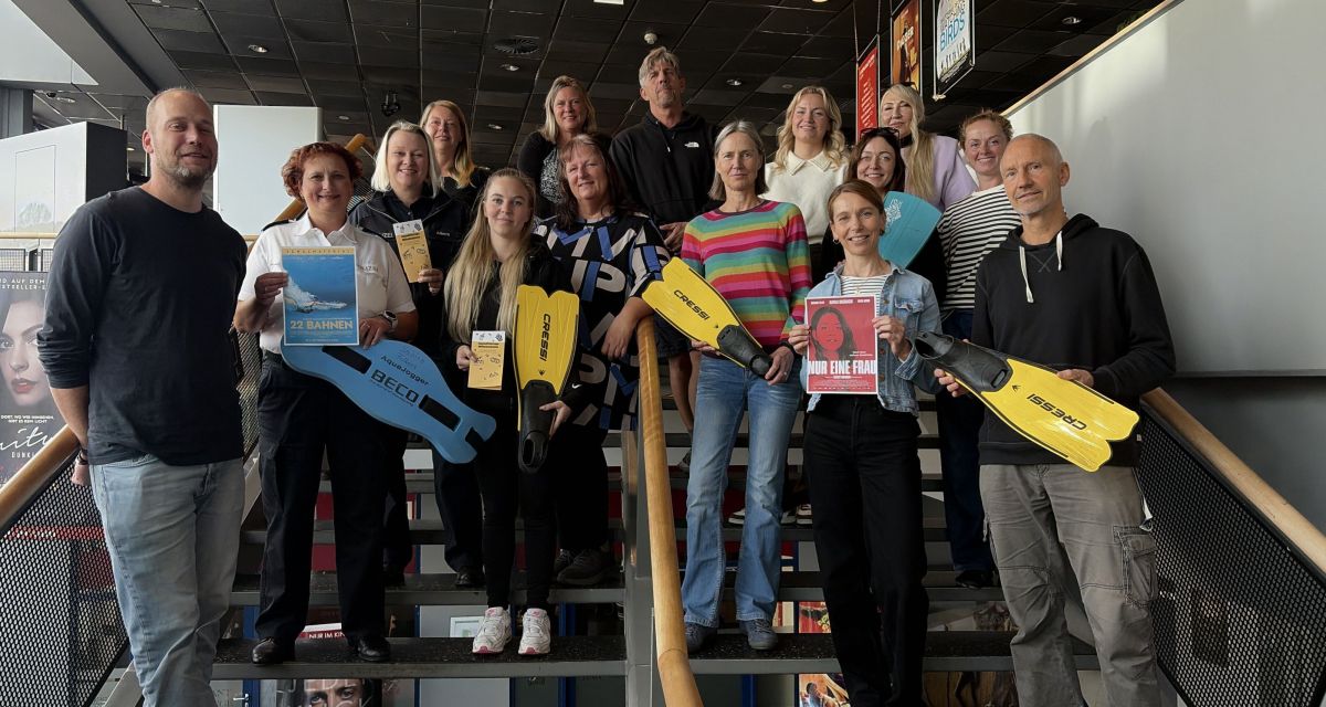 Auf der Treppe im Uci Kino in Wilhelmshaven stehen mehrere Mitgliedern der Arbeitsgruppe