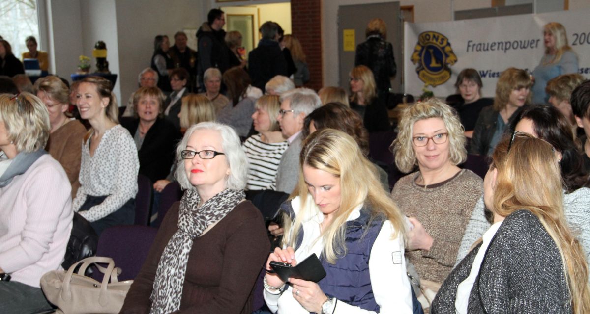 Verschiedene Frauen sitzen im Publikum und hören der Veranstaltung zu. Im Hintergrund Banner des Lion-Clubs. 