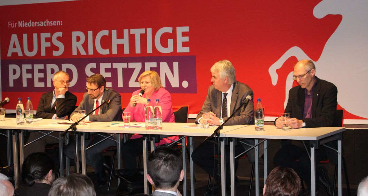 An einem Tisch sitzen in einer Reihe mehrere Politiker. Getränke auf dem Tisch. Im Hintergrund SPD-Banner. 