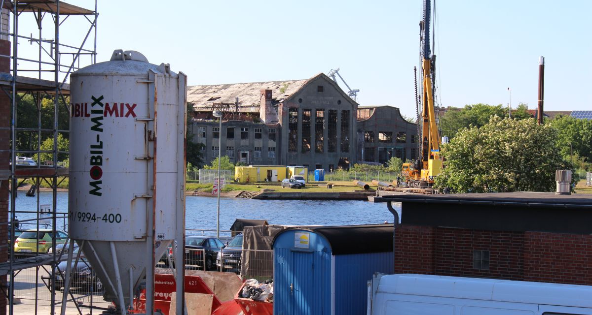 Im Hintergrund ein altes baufälliges Gebäude, vorne Baustelle. in der Mitte der Kanal.