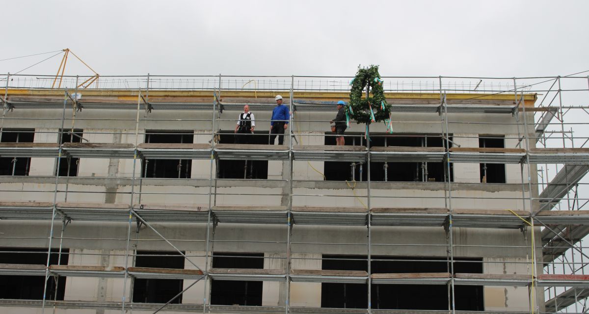 Drei Handwerker auf einem Gerüst neben einem Richtkranz. 