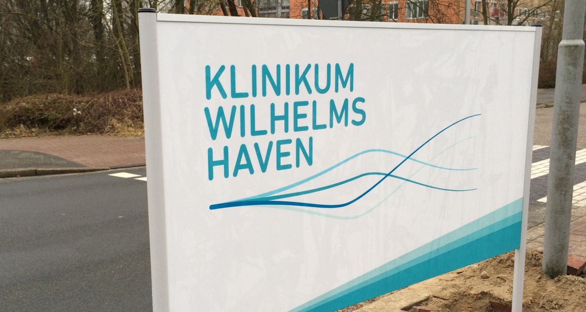 Zu sehen ist das Hinweisschild an der Zufahrt zum Klinikum Wilhelmshaven. In hellblauer Schrift steht auf dem weißen Schild