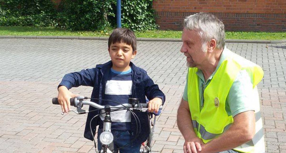 Ein Mann mit Sicherheitsweste kniet neben einem Jungen auf einem Fahrrad.