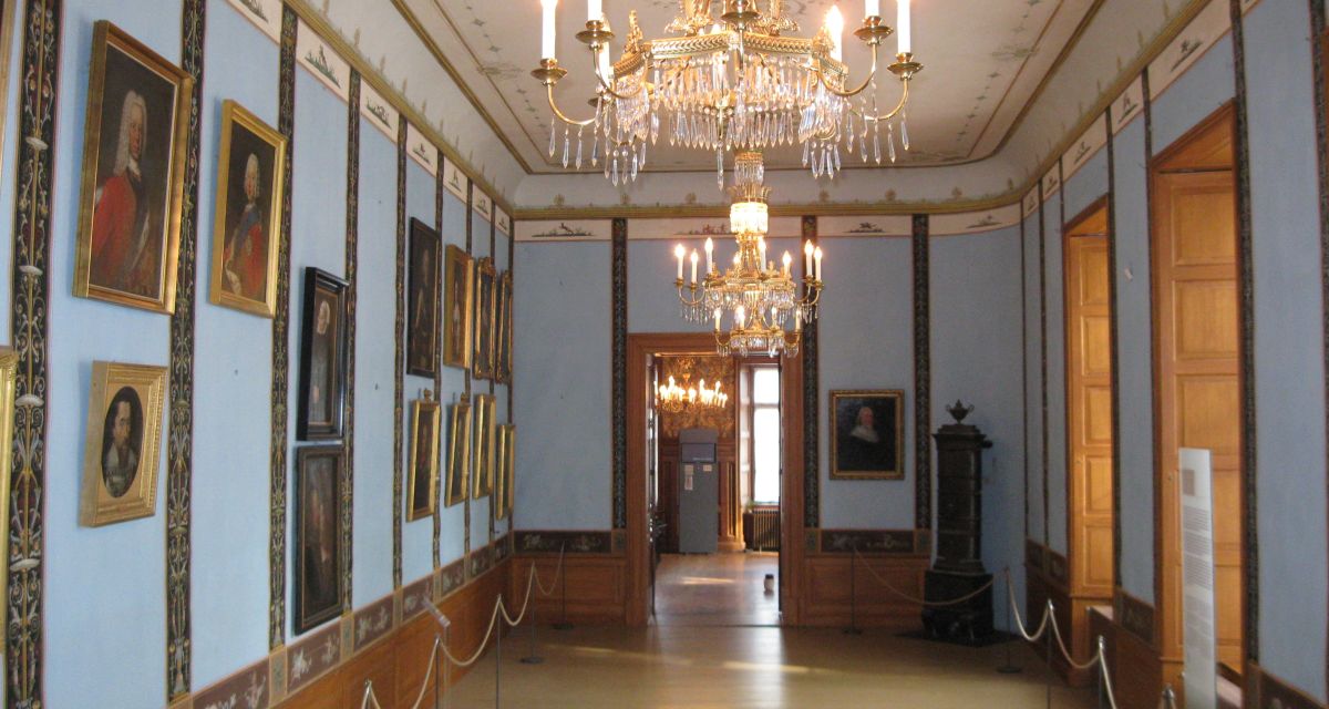 Innenansicht des Schlossmuseums Jever. Ein Saal mit einem großen Kronleuchter und vielen Goldapplikationen