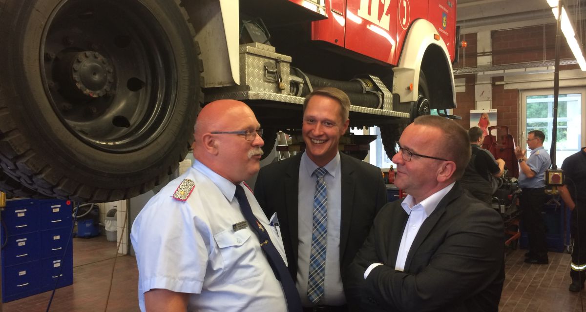 Boris Pistorius steht mit zwei anderen Männern in der Feuerwehrtechnischen Zentrale vor einem LKW, der sich auf einer Hebebühne befindet.