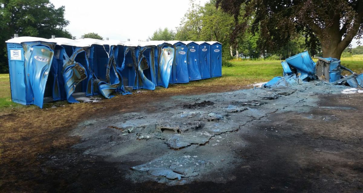 Es sind mehrere Toilettenhäuser zu sehenm die aufgrund des Feuers teilweise geschmolzen sind. Im Vordergrund ist eine große schwarze verrußte Fläche zu sehen.