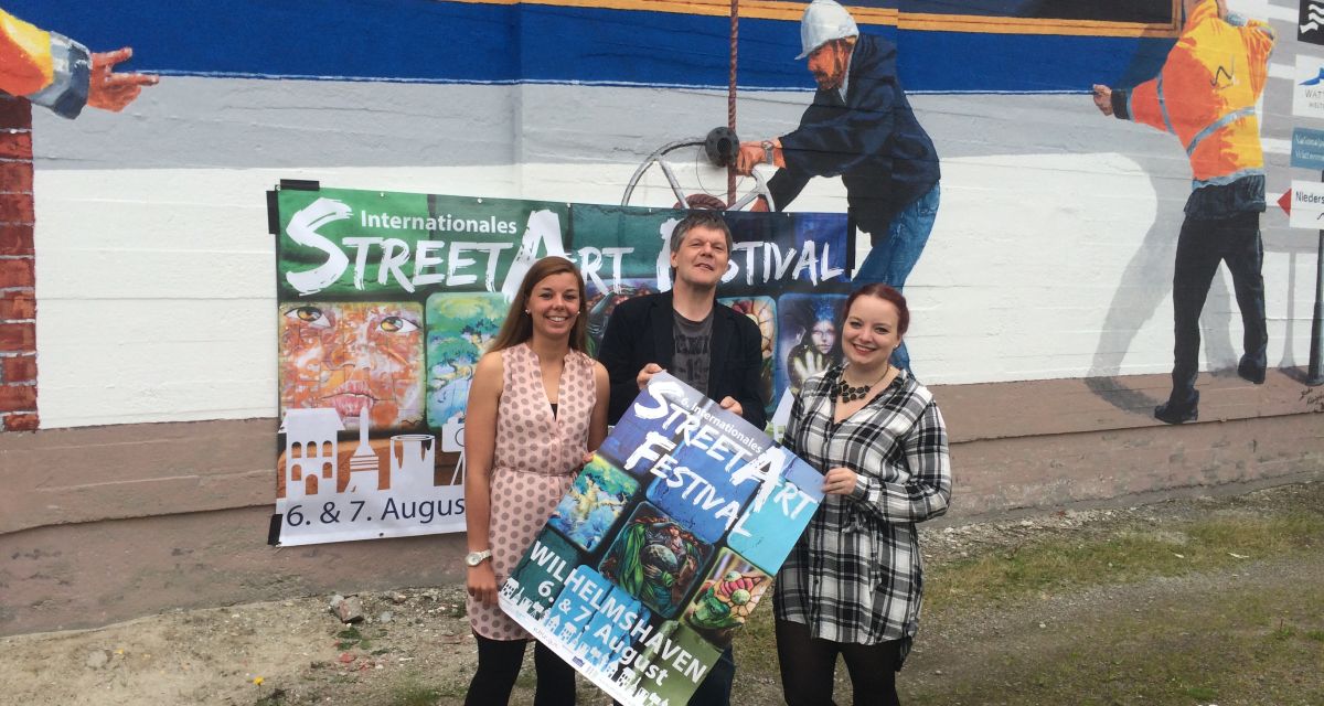 Michael Diers, Geschäftsführer der WTF mit zwei Frauen und dem Plakat für das Streetartfestival 2016 in Wilhelmshaven. 