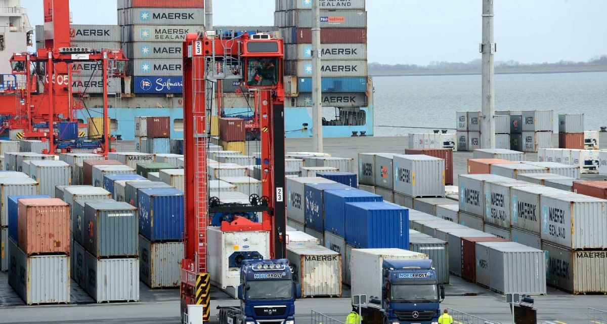 Im Vordergrund zwei Lkws. Dahinter viele Container. Im Hintergrund der Jade-Weser-Port und die Nordsee.