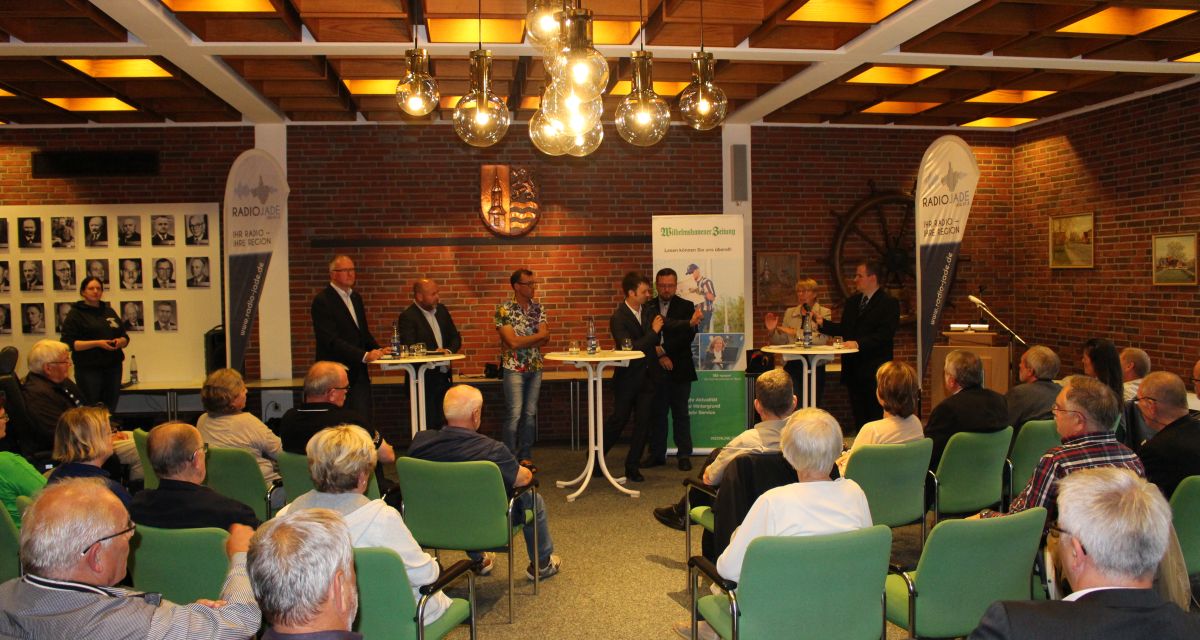 Zu sehen sind verschiedene Redner und ein Publikum bei einer Podiumsdiskussion im Rathaus in Sande.