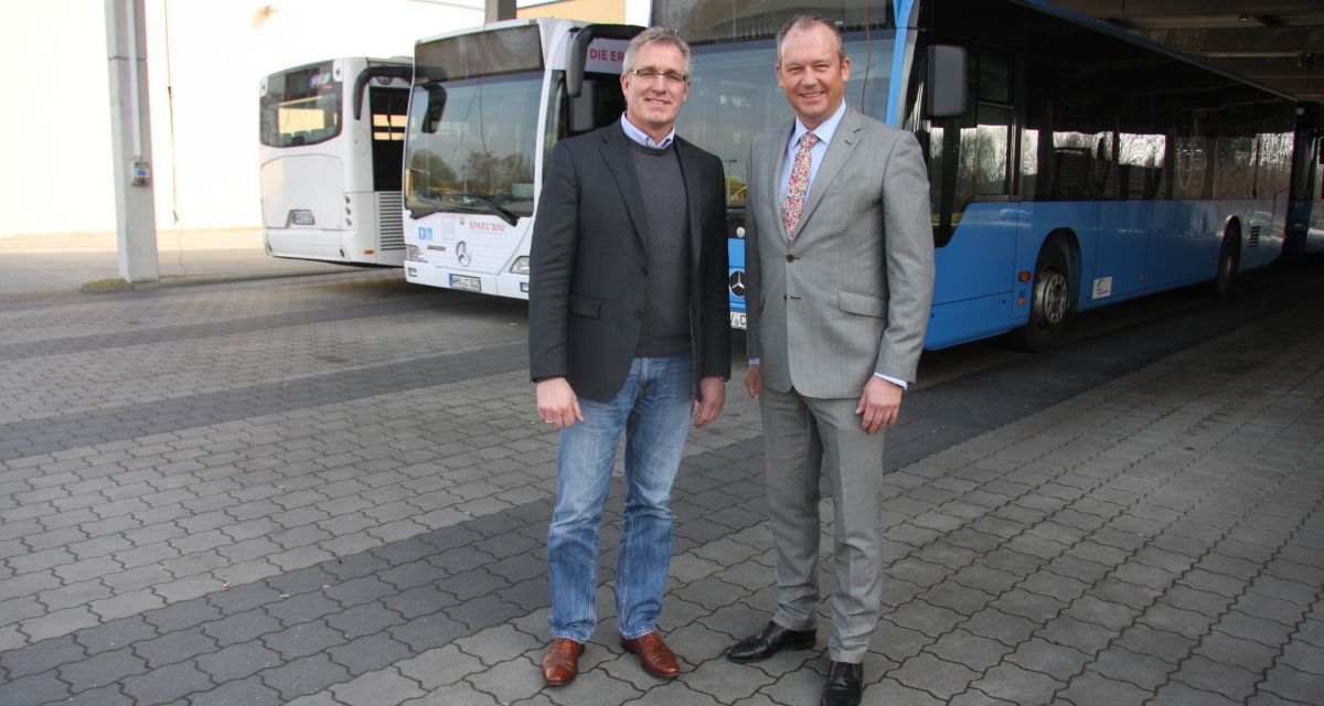 Zwei Männer posieren vor Bussen für die Kamera.