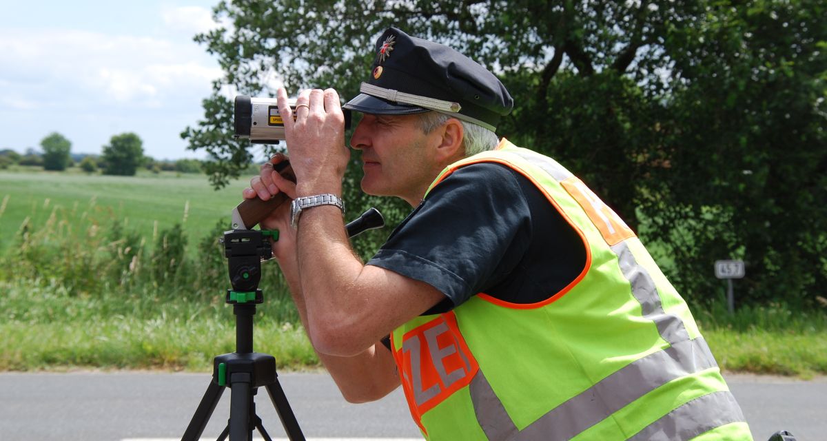 Zu sehen ist ein Polizeibeamter, während er durch ein Geschwindigkeits-Messgerät schaut.